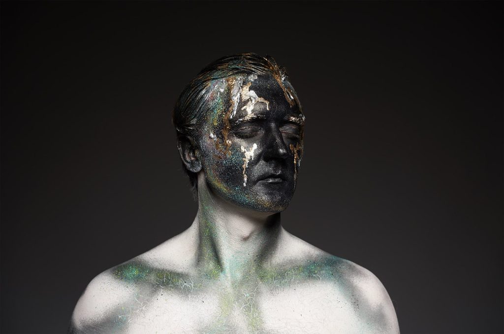A man with paint on his face with his eyes closed, depicting a character in a fantasy series.
