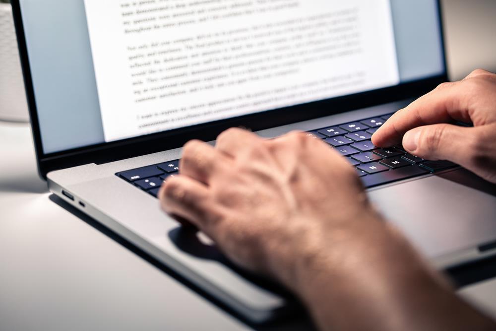 A person writing a text document on a laptop