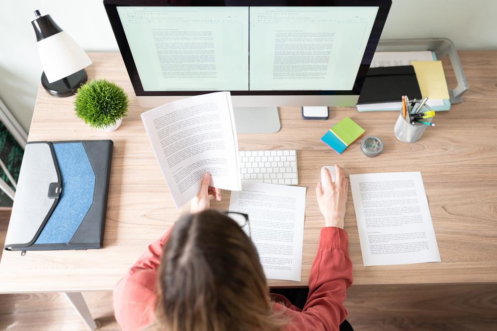 Top view of a workspace of a female working on a document and checking references in the computer